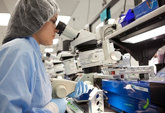 professional on clean suit looking through a microscope