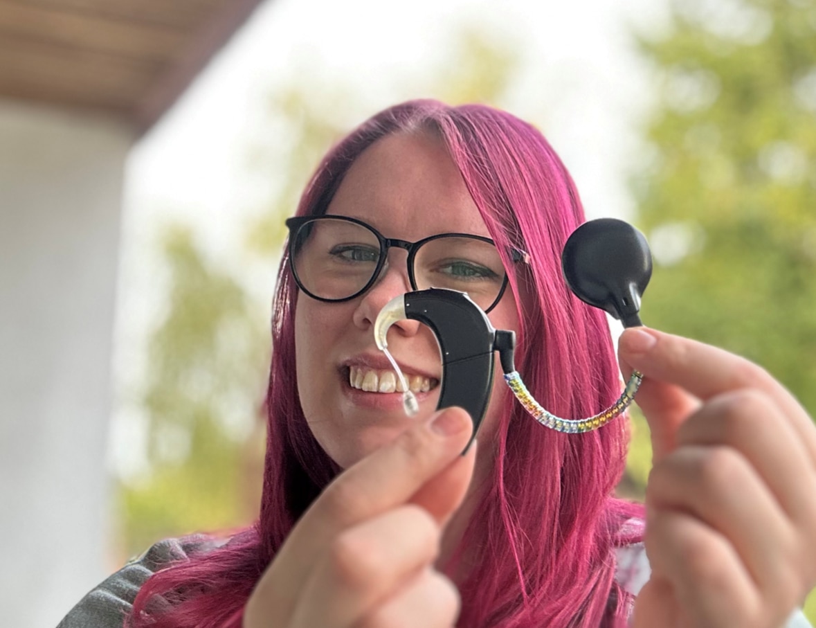 Luisa holding up her cochlear implant, sharing her experience living with a cochlear implant.