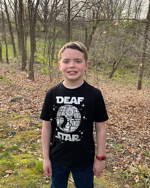 Jacob Schneider, a child who underwent bilateral hearing loss treatments, standing outside.
