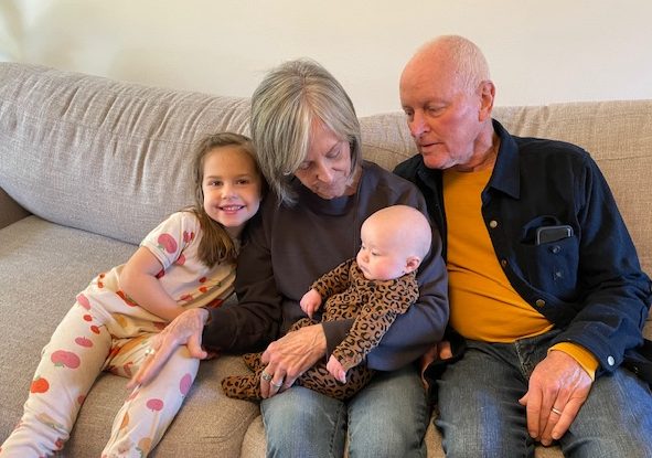 a grandmother holding a newborn child, sitting next to her husband, and her granddaughter