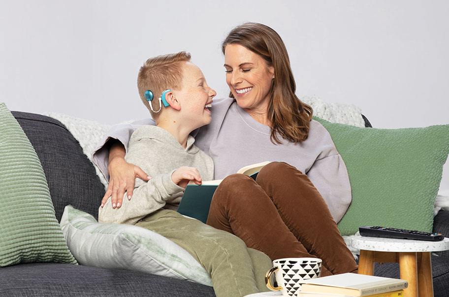 Photo of pediatric recipient, mother and son reading book on couch