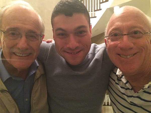 Two older men and one younger man join in a hug while smiling at the camera