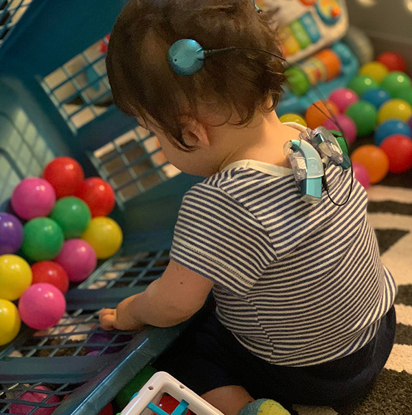 a baby playing with toys, they have two cochlear implants with processors clipped to their shirt