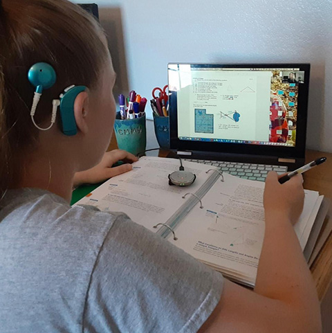girl with a cochlear implant does her homework in front of a computer 