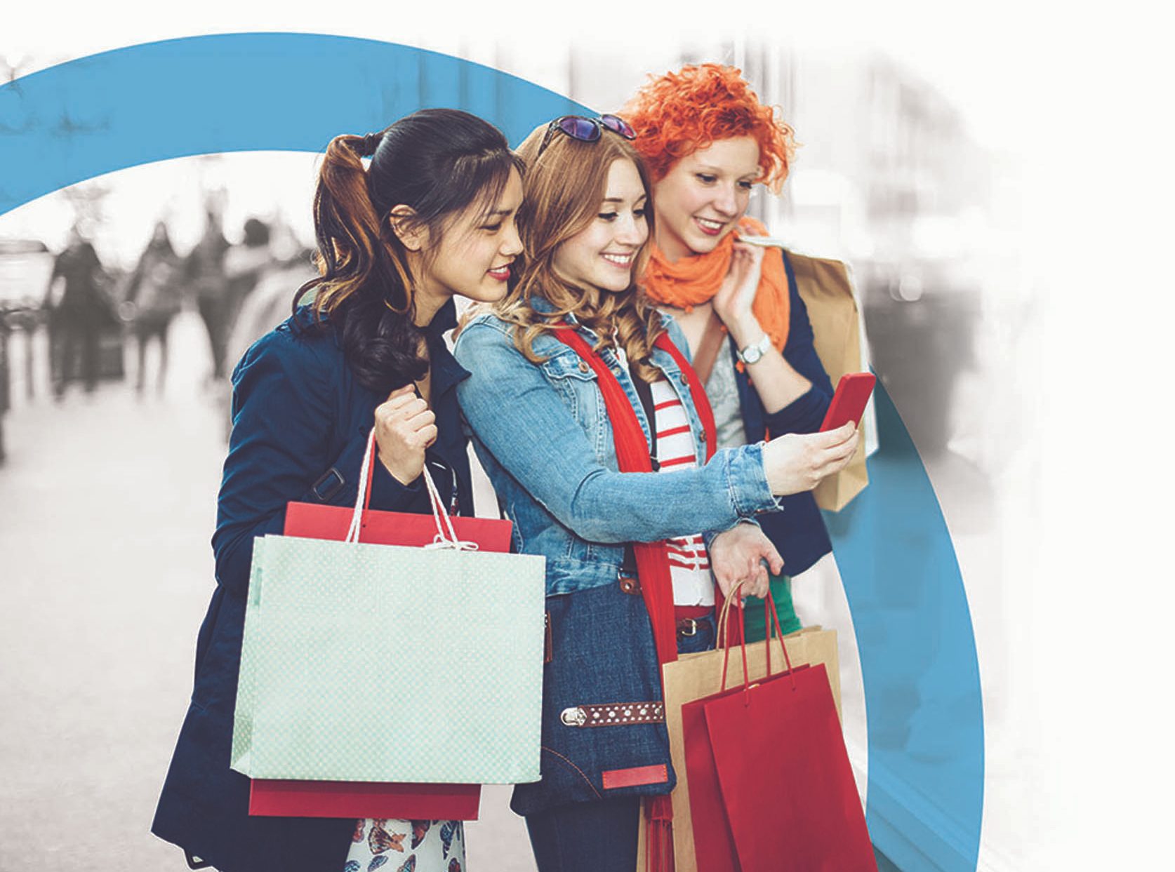 Multi-ethnic group is texting next to a shopping mall. The fashionable three women are holding shopping bags and laughing while they are using a smart phone. Outdoors candid shot.