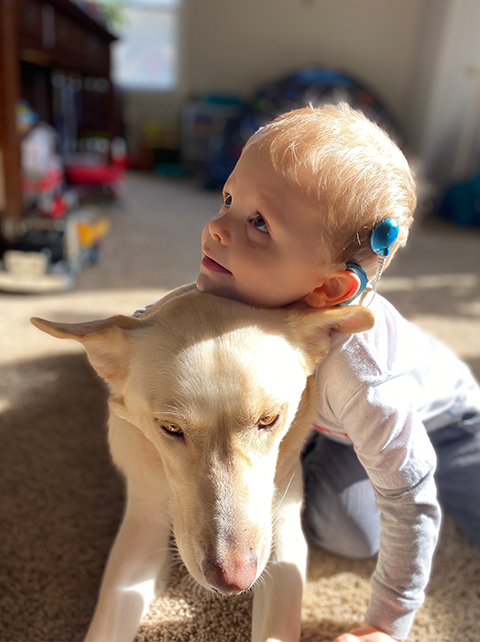 Child with cochlear implant cuddles with dog