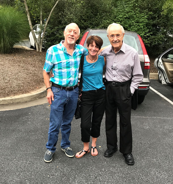 three mature people, two men and one woman, happily pose for a picture in a parking lot