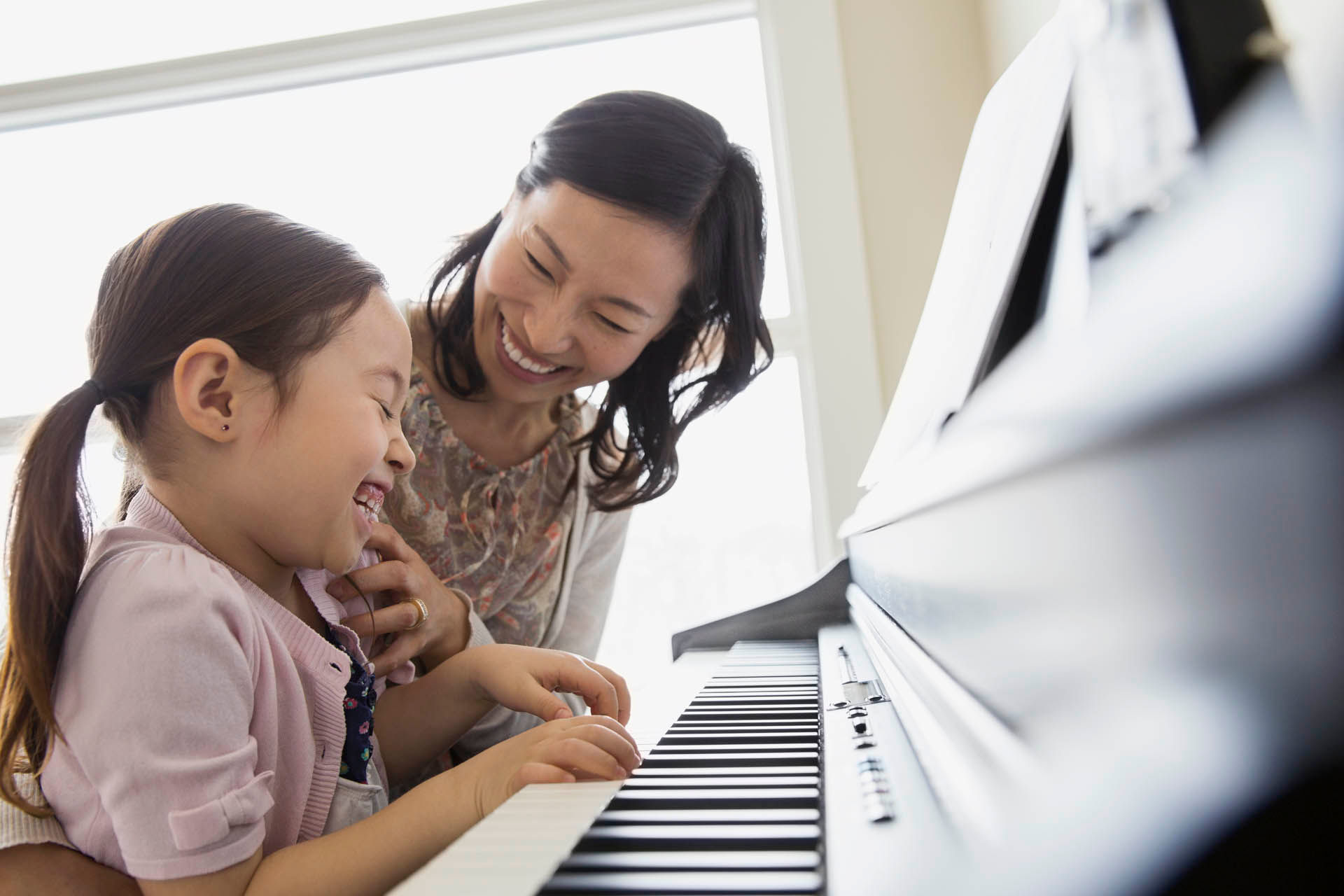 Daughter laughing and playing piano with mother 